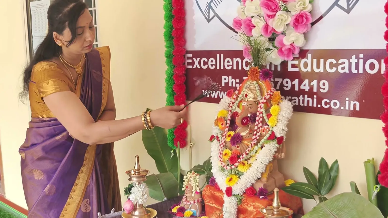 A woman in a sari offering prayers at a Ganesha idol decorated with garlands of flowers