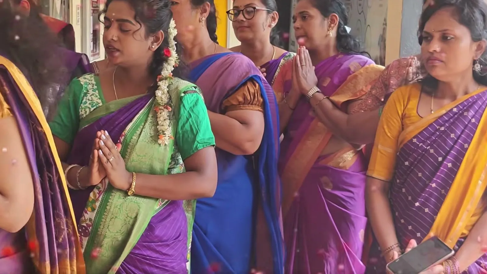 Women in saris standing in a line with their hands folded in prayer