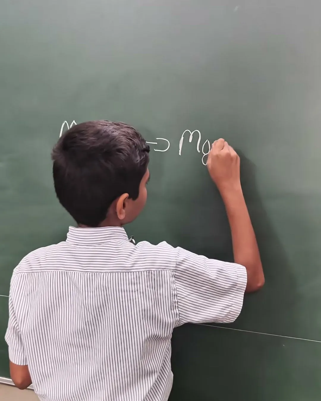 A student, seen from behind, writing a chemical equation for magnesium and oxygen on the blackboard
