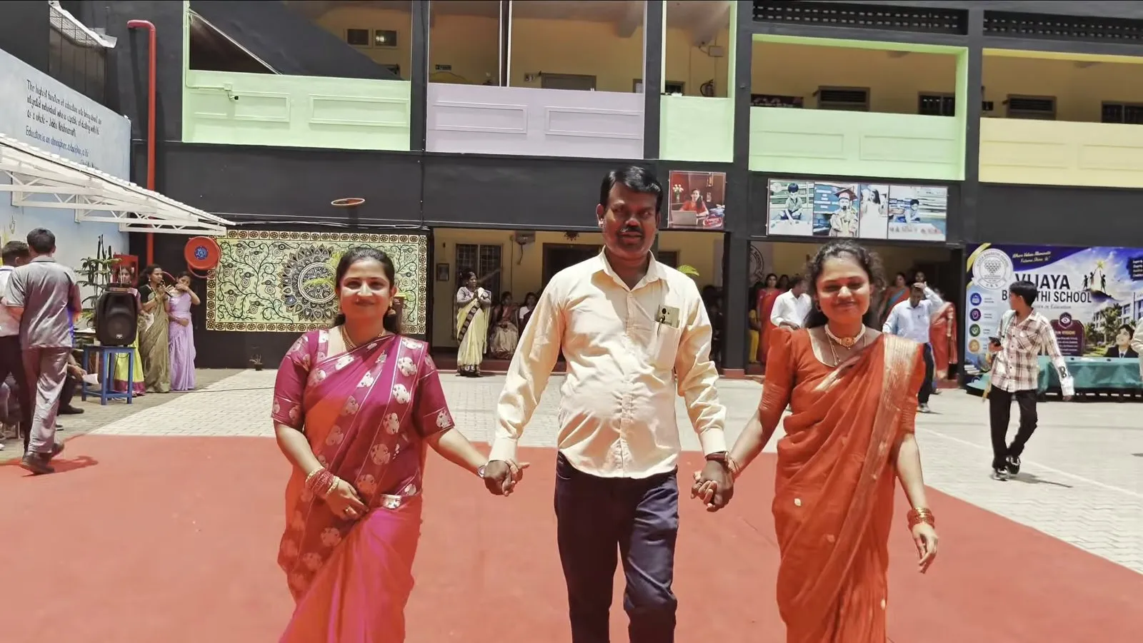 A man and two women in saris walking hand in hand along a red carpet in the courtyard