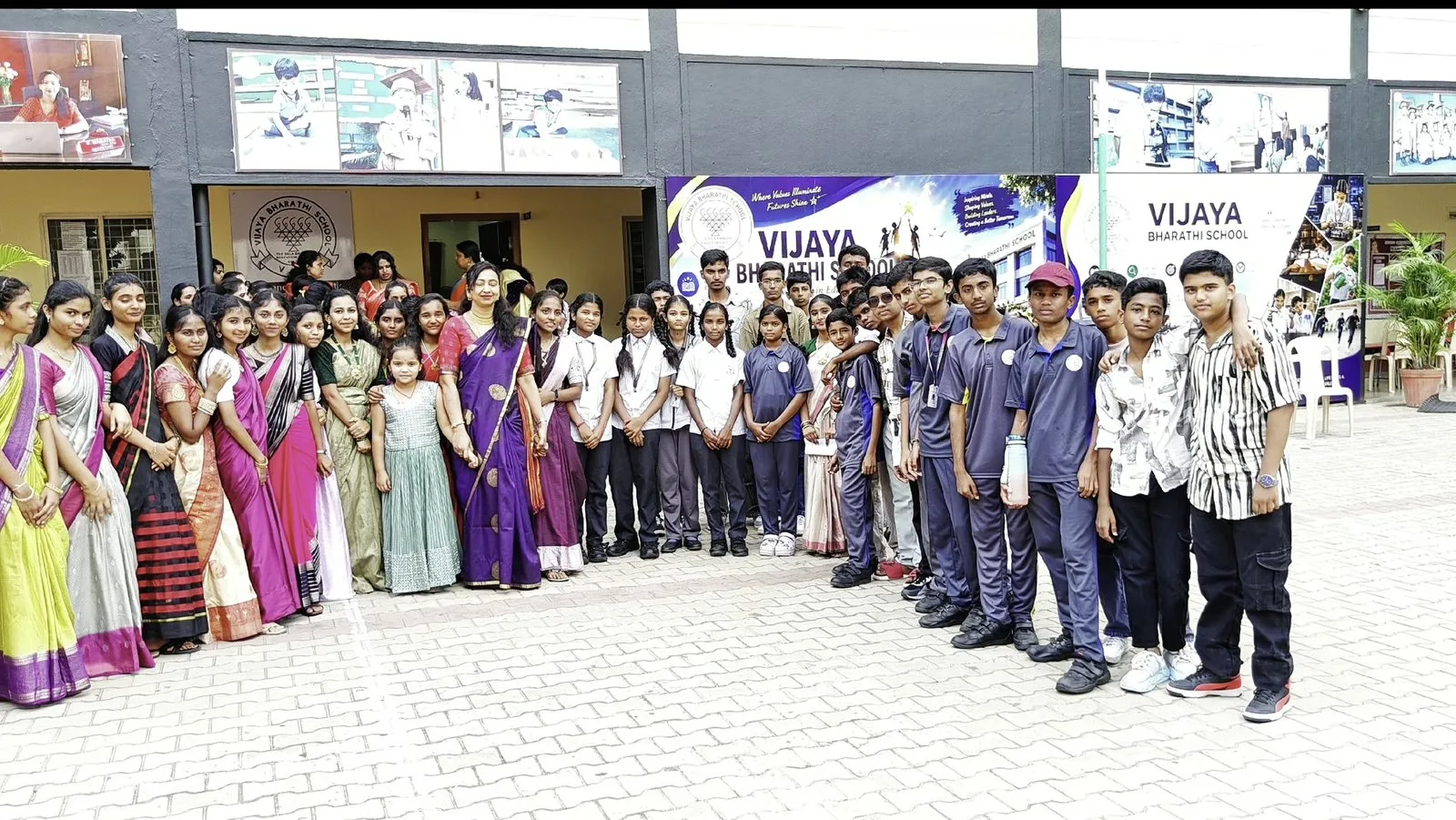 A large group of students and people in saris standing together for a photograph in the paved courtyard